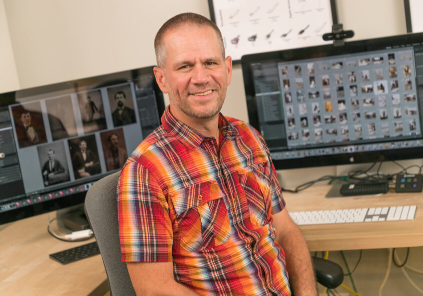 Adam Pratt in front of computers at a desk - Choose Chaos to Memories